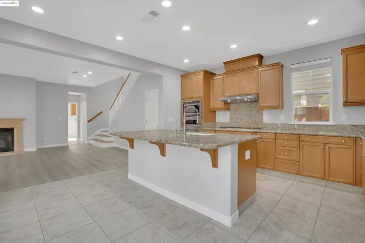 Kitchen featuring light tile patterned flooring, light stone counters, decorative backsplash, a breakfast bar, and a center island with sink