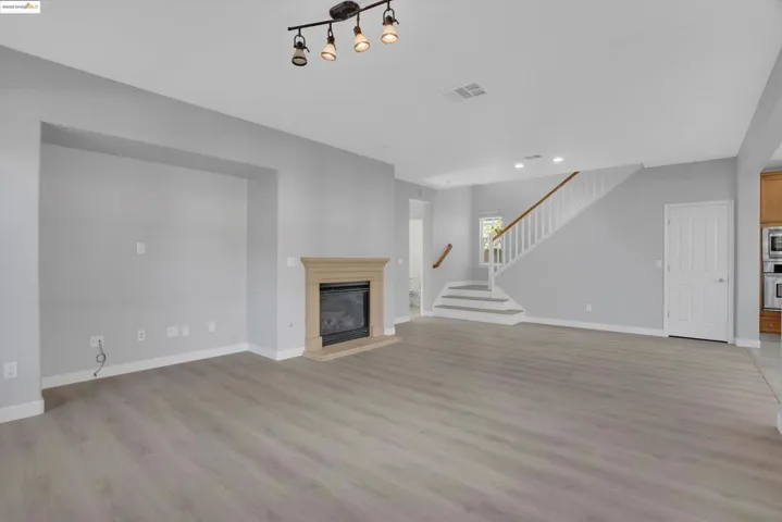 Unfurnished living room featuring light wood-type flooring, a glass covered fireplace, stairs, and recessed lighting