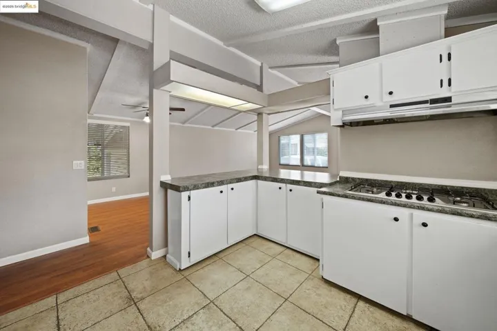 Kitchen with white cabinetry, lofted ceiling, a textured ceiling, light tile patterned floors, and a ceiling fan