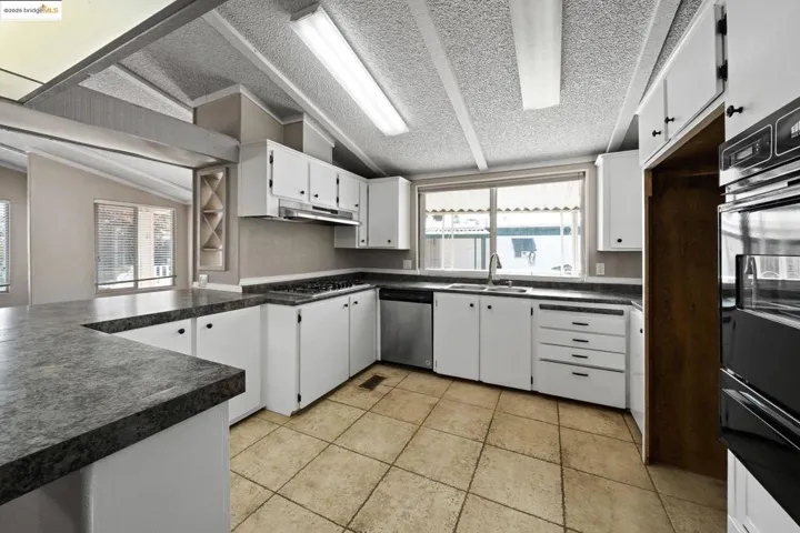 Kitchen with dark countertops, white cabinets, vaulted ceiling, a warming drawer, and stainless steel appliances