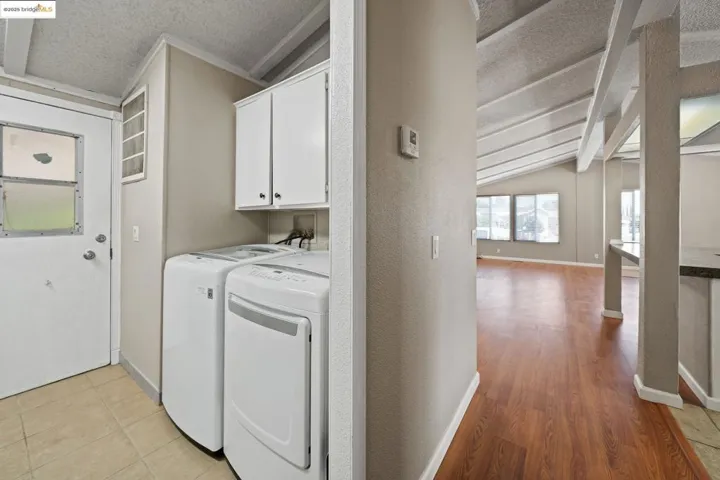 Laundry area with a textured ceiling, washer and dryer, light wood finished floors, and cabinet space
