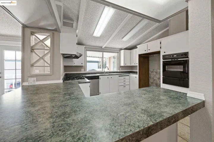 Kitchen with dark countertops, a peninsula, white cabinetry, black oven, and lofted ceiling