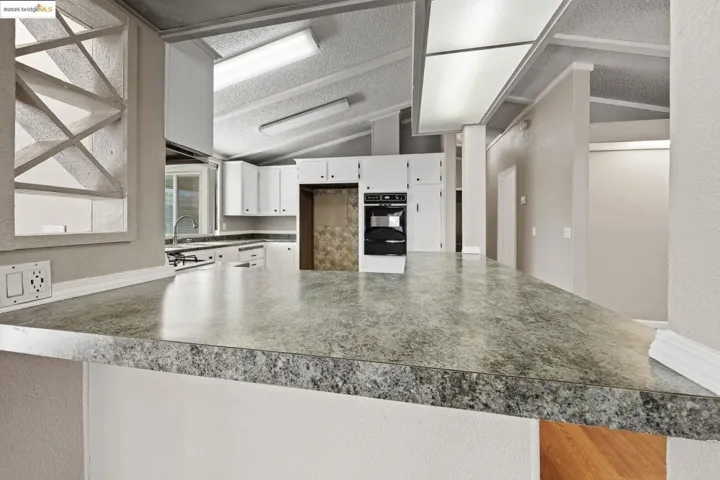 Kitchen with vaulted ceiling, a peninsula, a textured wall, white cabinetry, and black oven