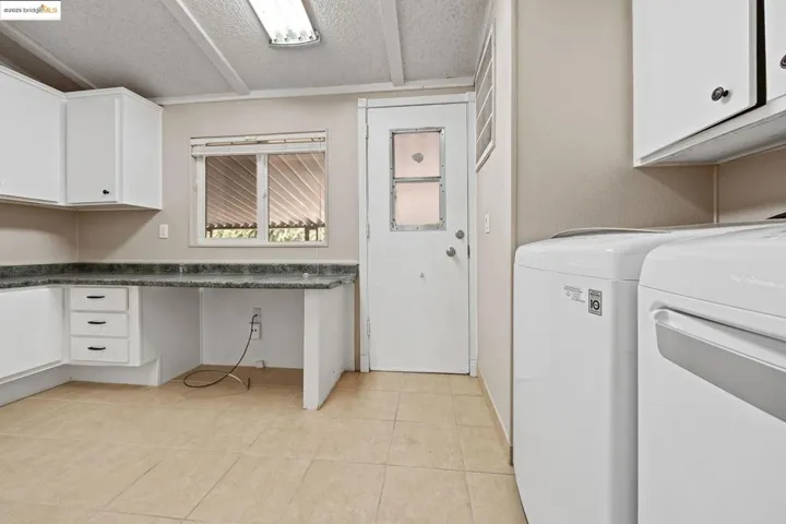 Washroom with cabinet space, light tile patterned floors, washing machine and dryer, and a textured ceiling