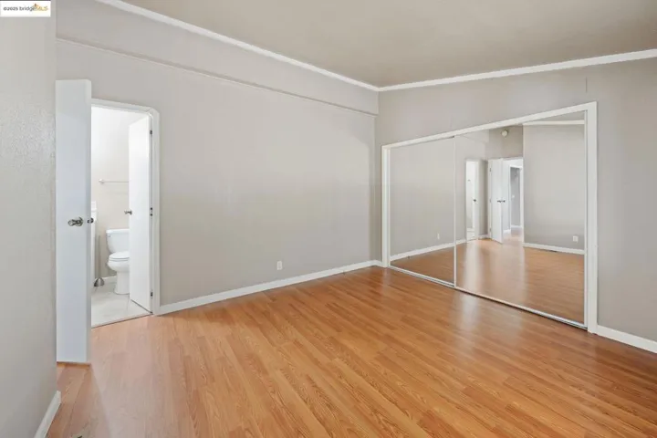Unfurnished bedroom with a closet, light wood finished floors, ornamental molding, and ensuite bathroom