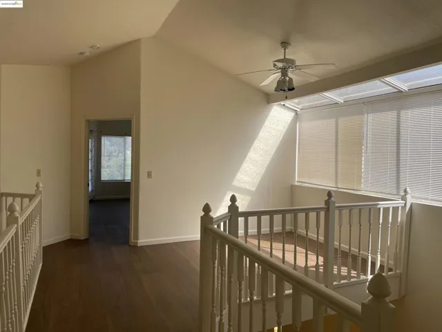 Corridor with an upstairs landing, dark wood-style flooring, and lofted ceiling