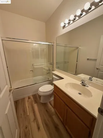 Full bath with enclosed tub / shower combo, vanity, and dark wood finished floors