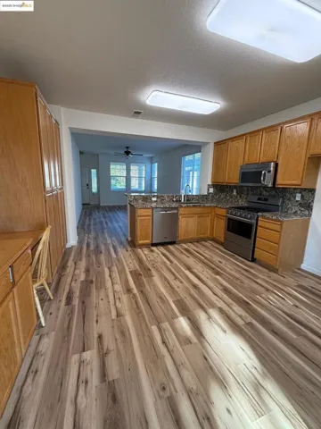 Kitchen with appliances with stainless steel finishes, a peninsula, brown cabinetry, dark stone counters, and a textured ceiling