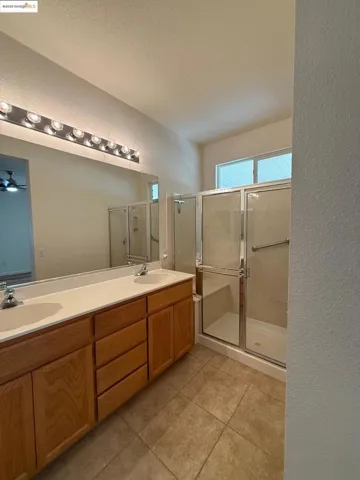 Full bathroom featuring a textured wall, a stall shower, double vanity, light tile patterned floors, and a textured ceiling