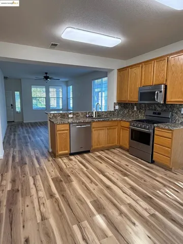 Kitchen featuring stainless steel appliances, tasteful backsplash, dark stone counters, brown cabinetry, and light wood-style flooring