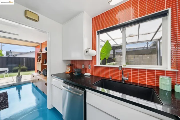 Kitchen with dishwasher, white cabinets, dark stone countertops, finished concrete flooring, and tasteful backsplash