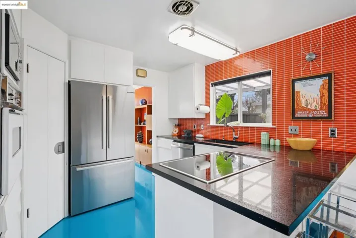 Kitchen with white cabinets, stainless steel appliances, a peninsula, dark countertops, and decorative backsplash