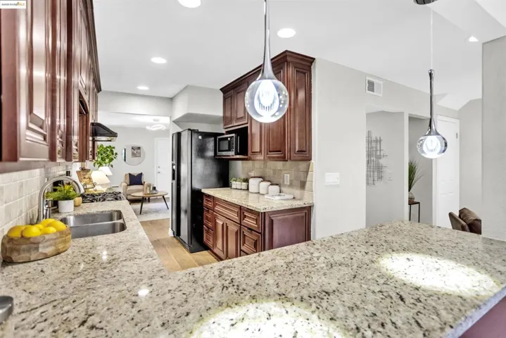 Kitchen with light stone counters, recessed lighting, backsplash, black refrigerator with ice dispenser, and hanging light fixtures