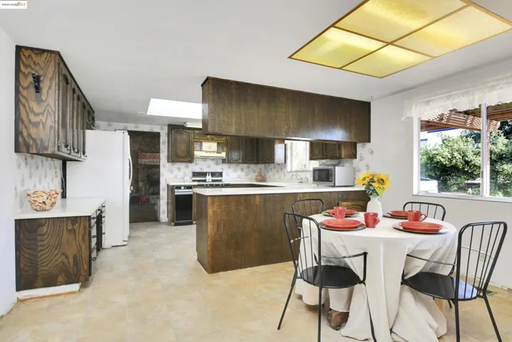Kitchen with dark brown cabinets, light countertops, freestanding refrigerator, a skylight, and a peninsula