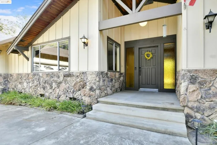 Property entrance with stone siding, board and batten siding, and covered porch