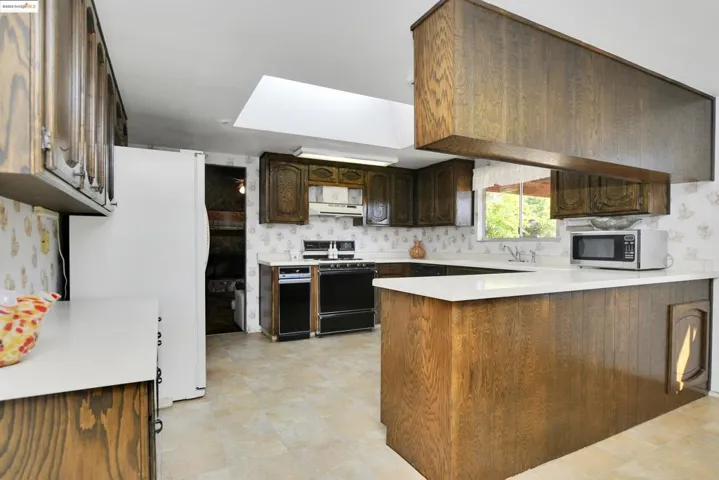 Kitchen with wallpapered walls, light countertops, freestanding refrigerator, a peninsula, and stainless steel microwave