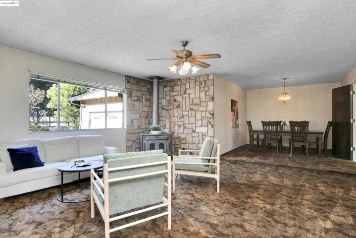 Living area featuring a wood stove, dark carpet, a textured ceiling, a ceiling fan, and a chandelier