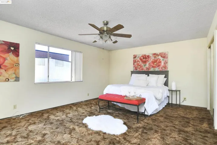 Bedroom with a textured ceiling, carpet flooring, and a ceiling fan