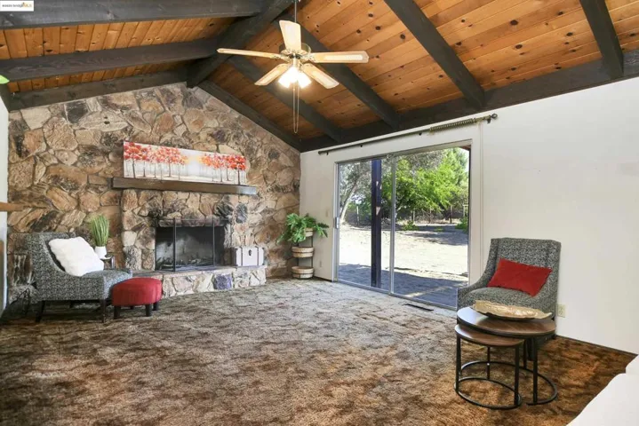 Sitting room with carpet, a fireplace, high vaulted ceiling, a ceiling fan, and a wooden ceiling with exposed beams