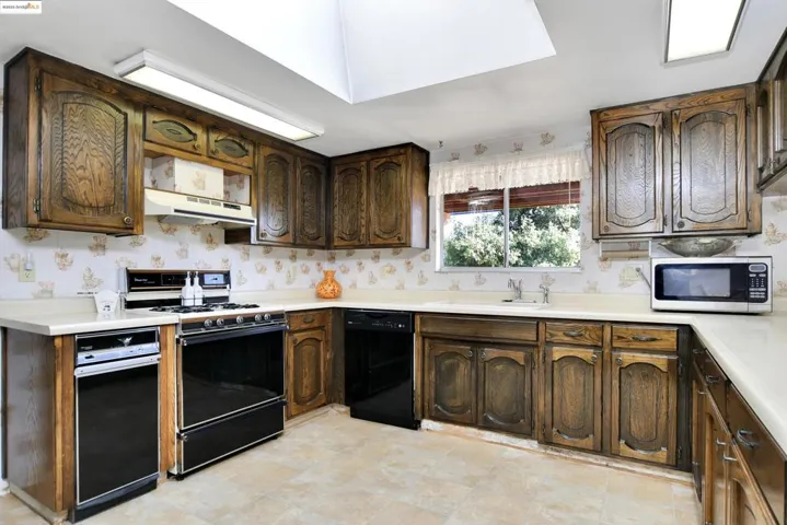 Kitchen with range with electric stovetop, light countertops, black dishwasher, under cabinet range hood, and dark brown cabinets