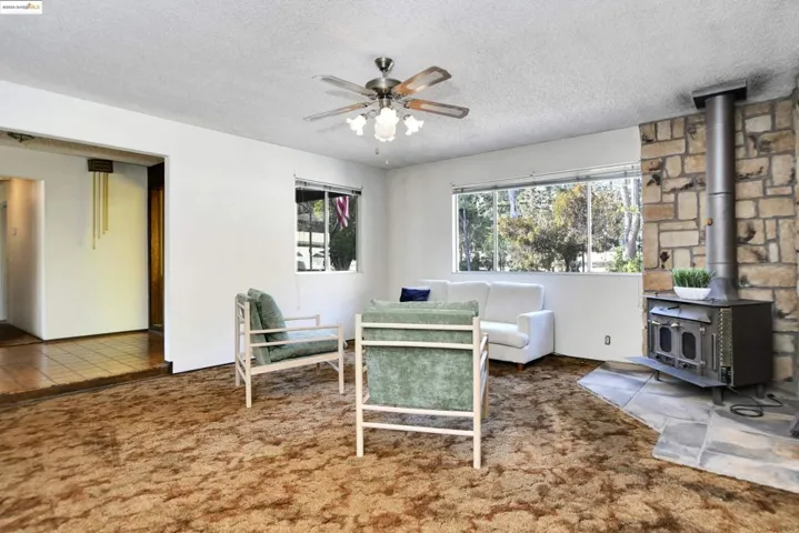Living room featuring a wood stove, carpet floors, a textured ceiling, and a ceiling fan