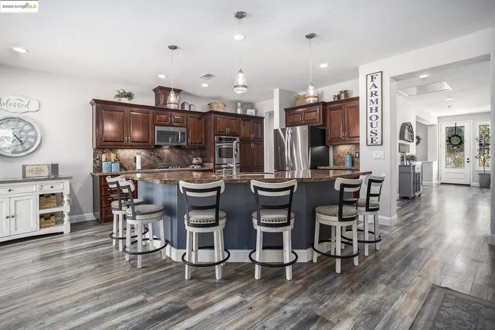 Kitchen featuring tasteful backsplash, dark cabinetry, hanging light fixtures, an island with sink, and recessed lighting