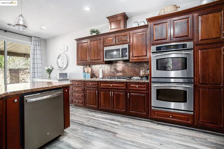 Kitchen featuring appliances with stainless steel finishes, double oven, 5 gas burner stovetop, tasteful backsplash, stone countertops, laminate wood-style floors, and pendant lighting