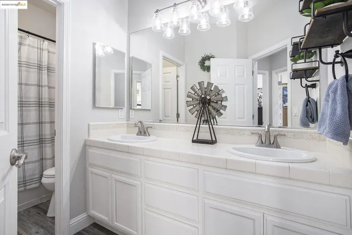 Full bath with double vanity and laminate wood-type flooring, with door separation of vanity and shower.