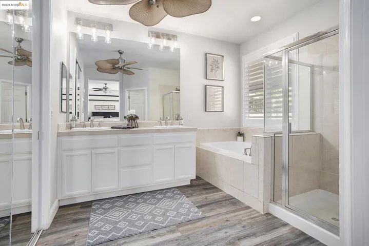 Bathroom with a bath, a shower stall, double vanity, laminate wood finished floors, and recessed lighting
