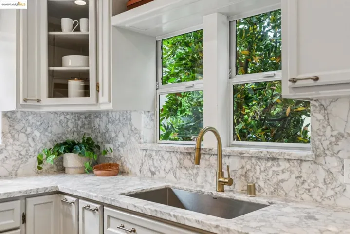 Kitchen with tasteful backsplash, light stone countertops, glass insert cabinets, and white cabinetry