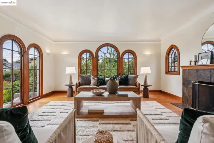 Living area featuring plenty of natural light, a tiled fireplace, light wood-style flooring, and ornamental molding