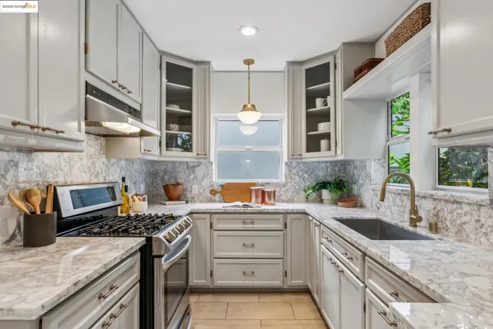 Kitchen featuring gas stove, pendant lighting, light stone counters, light tile patterned floors, and under cabinet range hood