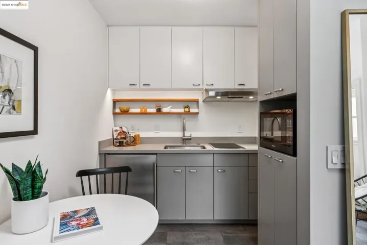 Bar area with open shelves, gray cabinets, black microwave, under cabinet range hood, and electric cooktop