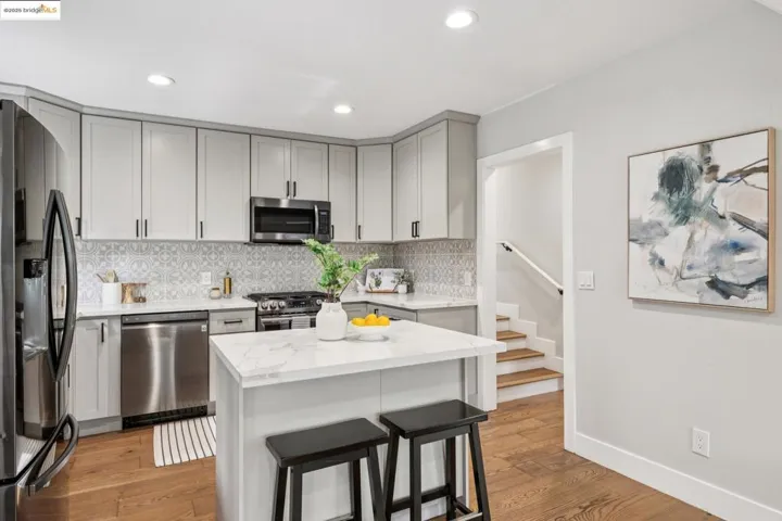 Kitchen featuring decorative backsplash, light stone countertops, appliances with stainless steel finishes, light wood-type flooring, and a breakfast bar area
