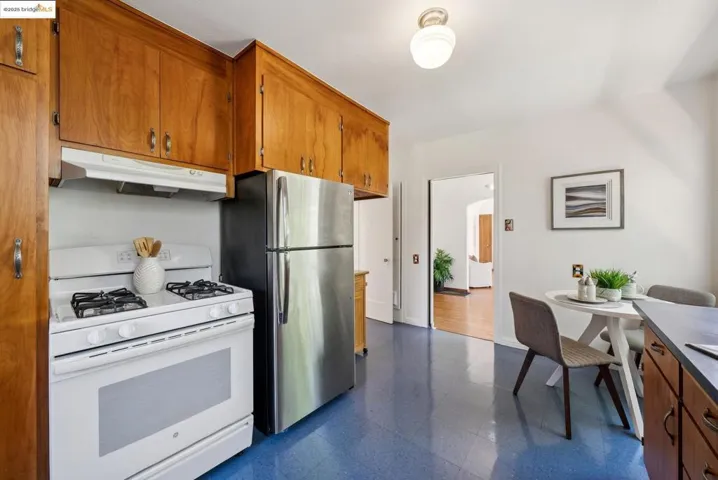Kitchen with gas range gas stove, brown cabinets, under cabinet range hood, dark flooring, and freestanding refrigerator
