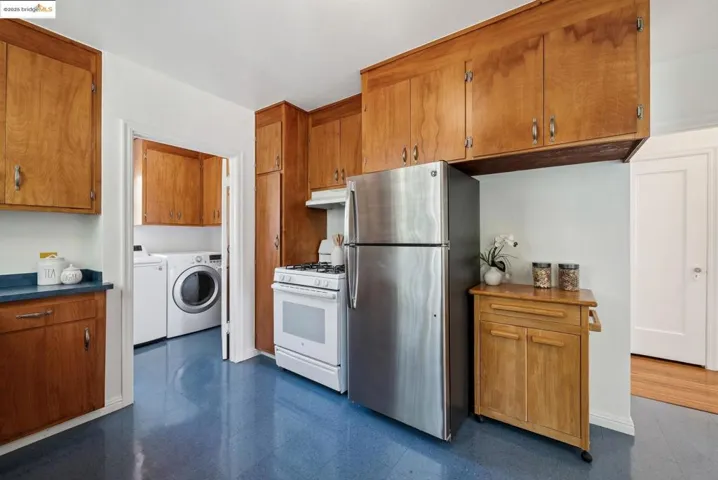 Kitchen with brown cabinets, freestanding refrigerator, dark flooring, white range with gas cooktop, and washer and clothes dryer