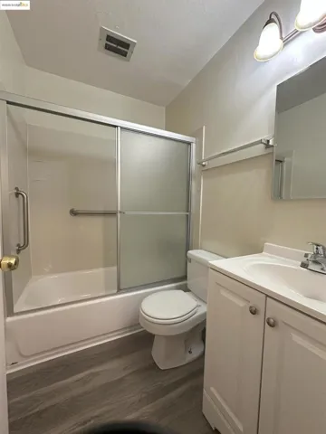 Bathroom featuring combined bath / shower with glass door, vanity, and dark wood-style floors