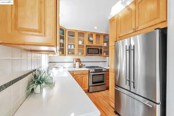 Kitchen featuring appliances with stainless steel finishes, glass insert cabinets, backsplash, light wood-type flooring, and recessed lighting
