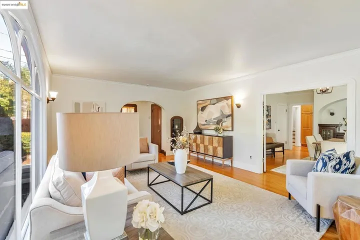 Living area with arched walkways, wood finished floors, and ornamental molding