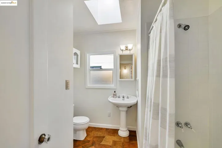 Full bathroom featuring a skylight, shower / bathtub combination with curtain, and dark stone finish floors