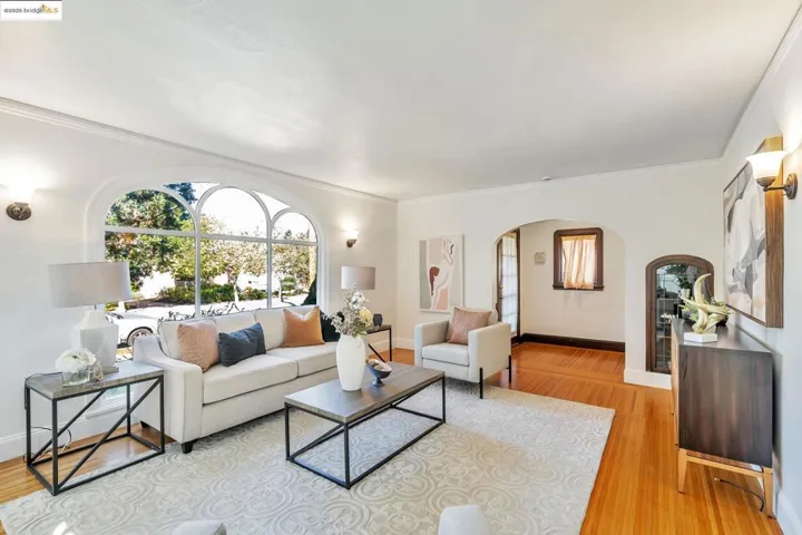 Living area with arched walkways, ornamental molding, and light wood-style flooring