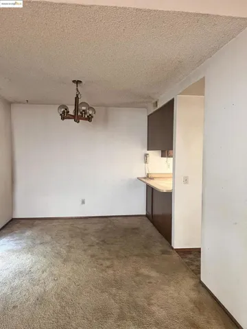 Unfurnished dining area featuring a chandelier, a textured ceiling, and dark colored carpet