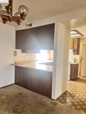 Kitchen with light countertops, a textured ceiling, electric stove, dark carpet, and a chandelier