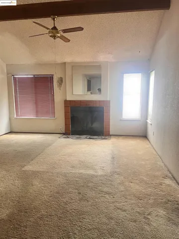 Unfurnished living room featuring a textured ceiling, a fireplace, carpet, ceiling fan, and a textured wall