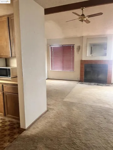 Unfurnished living room with dark colored carpet, ceiling fan, a fireplace with flush hearth, and a textured ceiling