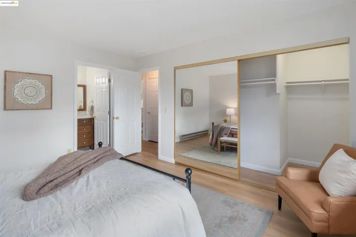 Bedroom featuring wood finished floors, baseboard heating, a closet, and connected bathroom