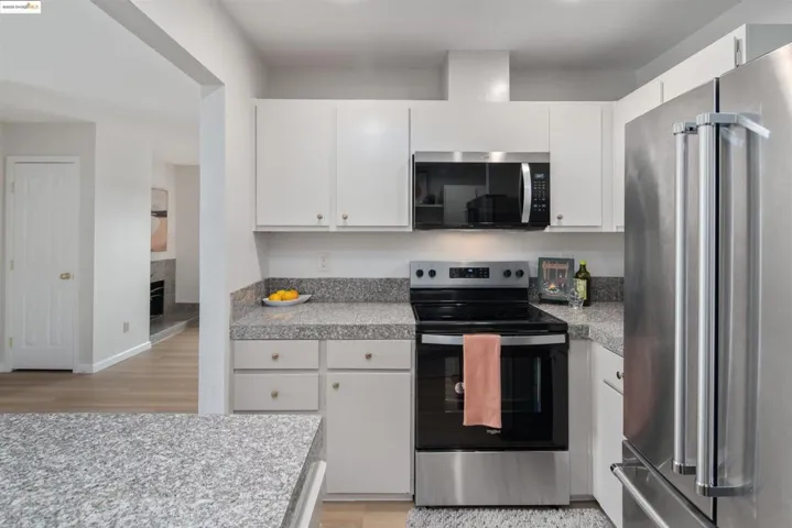 Kitchen featuring appliances with stainless steel finishes, white cabinets, light wood-style flooring, and tile countertops