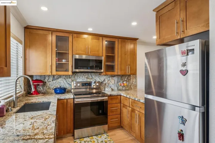 Kitchen featuring appliances with stainless steel finishes, brown cabinets, glass insert cabinets, tasteful backsplash, and light stone countertops
