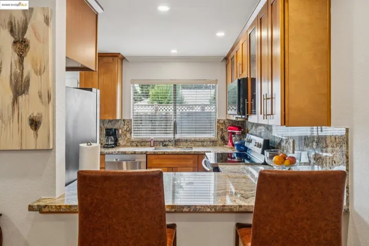 Kitchen with brown cabinetry, backsplash, light stone counters, stainless steel appliances, and a textured wall