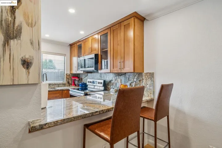 Kitchen featuring a textured wall, tasteful backsplash, light stone countertops, glass insert cabinets, and a kitchen bar